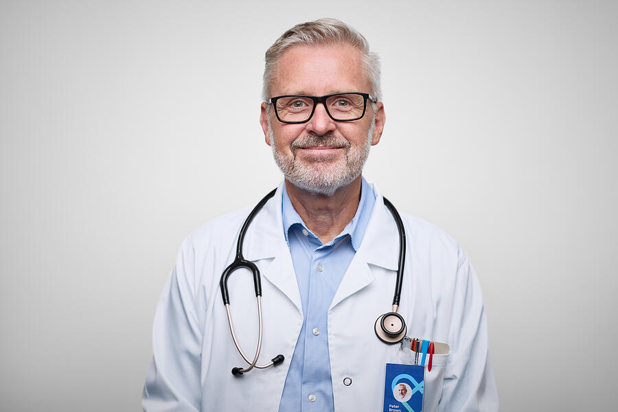 A male doctor with glasses, wearing a white coat and stethoscope, smiling.