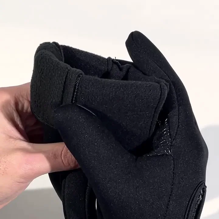 A hand holds a black glove, turning it to show the soft, fleece-like interior lining.