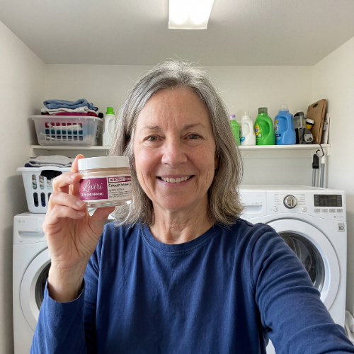 A smiling woman in a blue shirt holds a small jar in a laundry room.