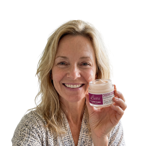 A smiling blonde woman in a patterned robe holds up a small jar of skin cream.
