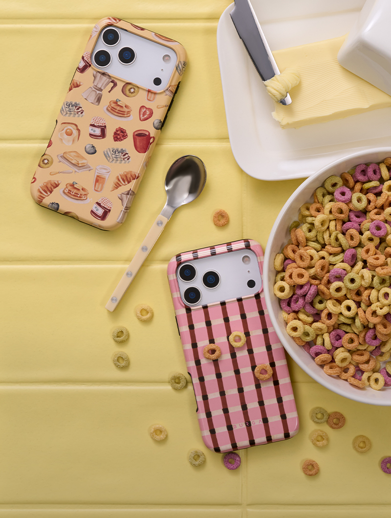 Two iPhones in decorative cases next to a bowl of cereal and a butter dish on a yellow table.
