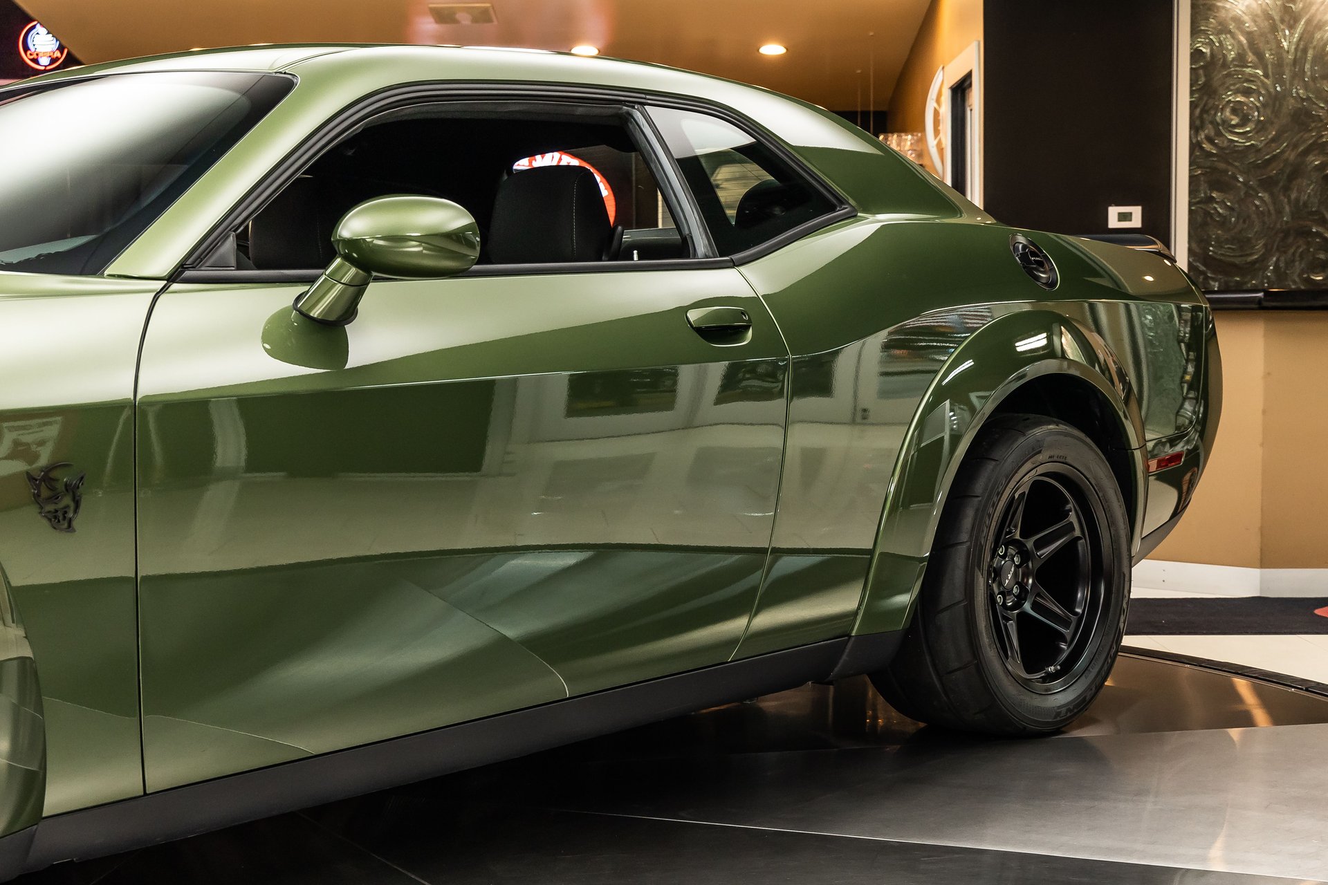 Side profile of a glossy, dark green Dodge Challenger on a reflective showroom floor.