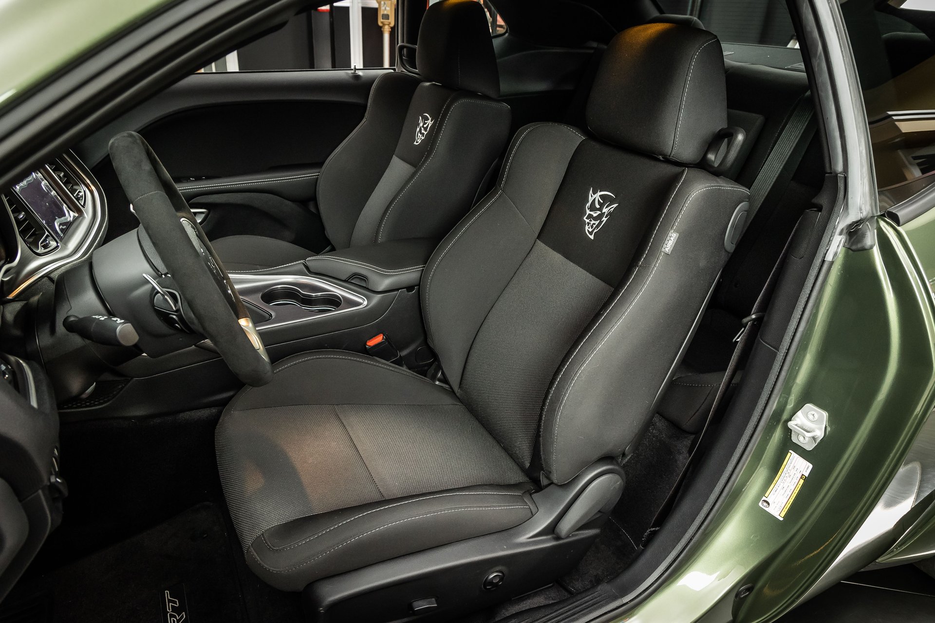 The front interior of a green car showing black cloth seats with an embroidered demon head logo.