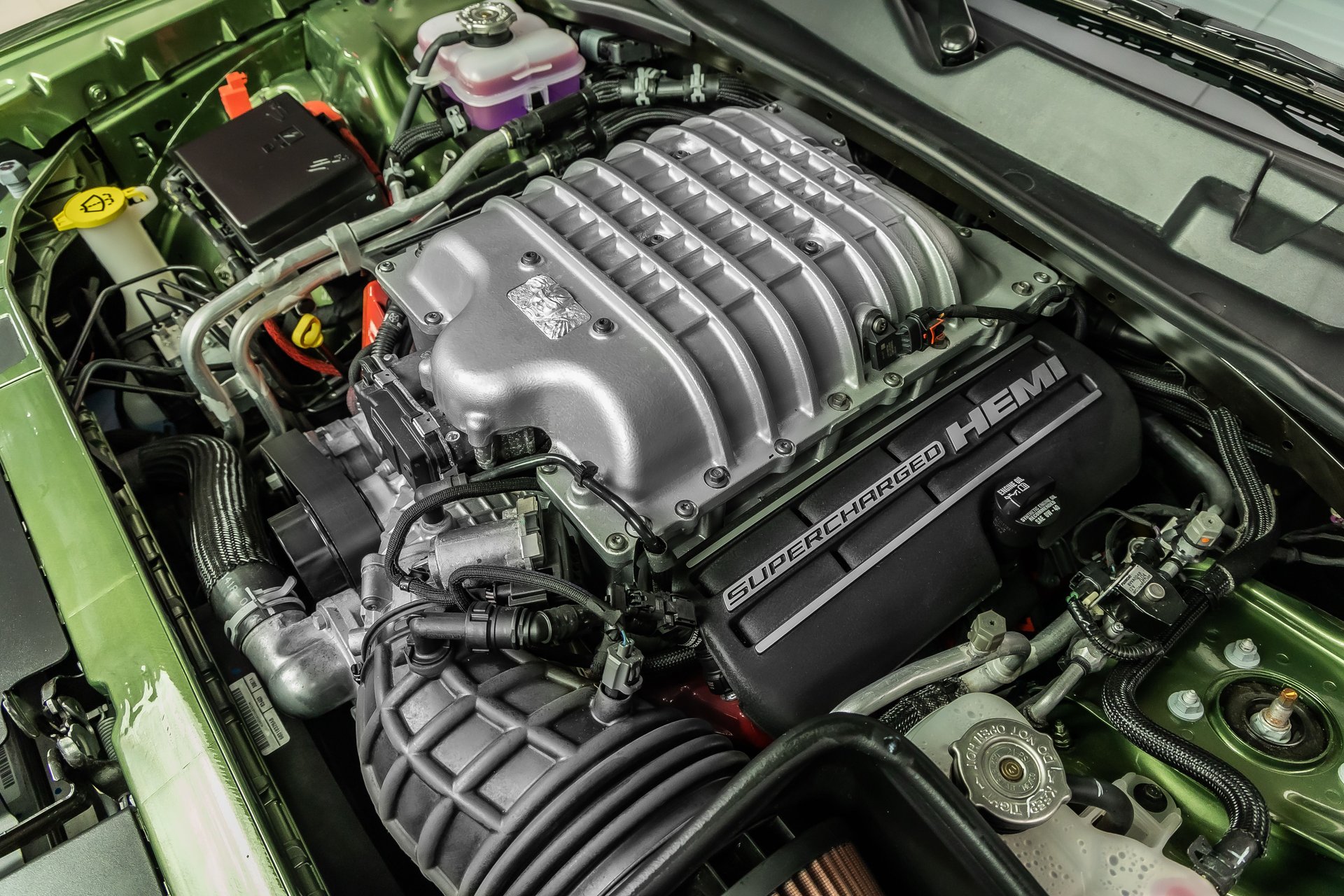 A close-up of a silver Supercharged HEMI engine inside a green car's engine bay.