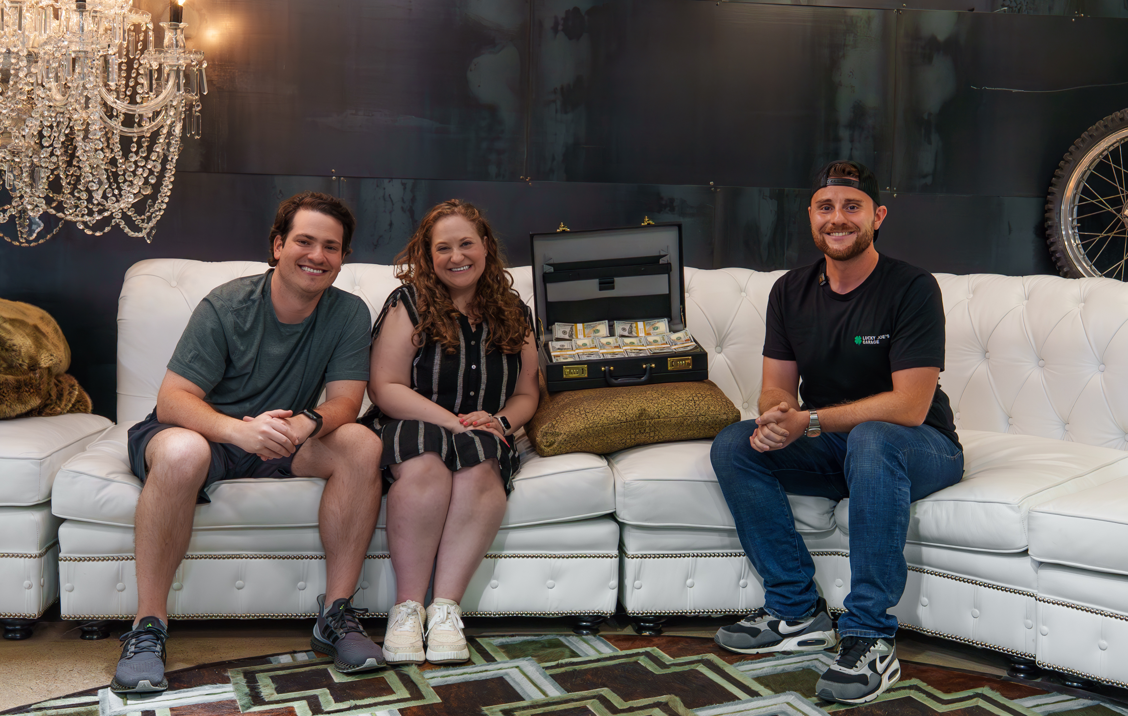 Three people sitting on a white couch with a briefcase of money.