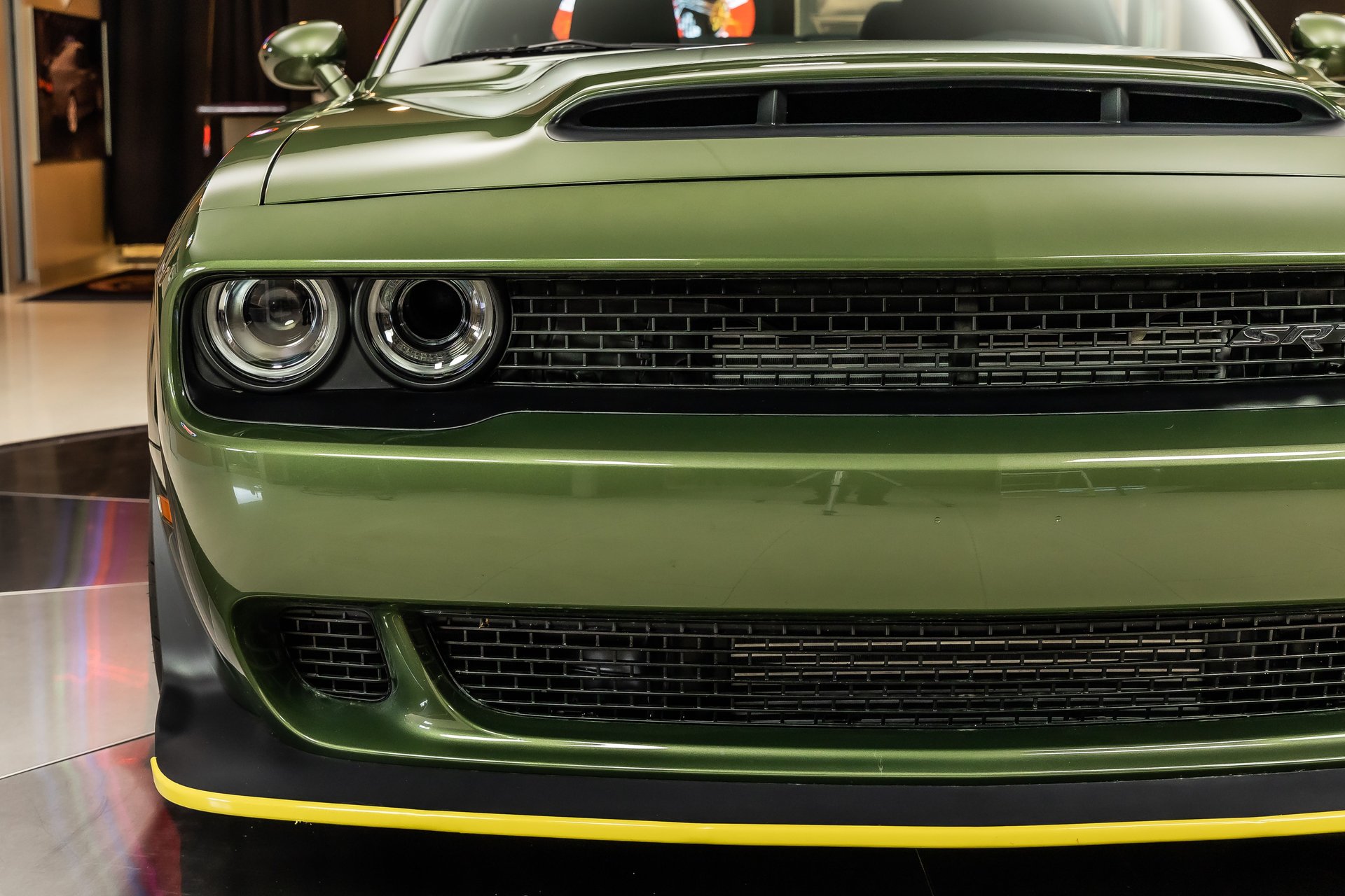 A close-up head-on shot of a green muscle car's front grille, headlights, and hood.