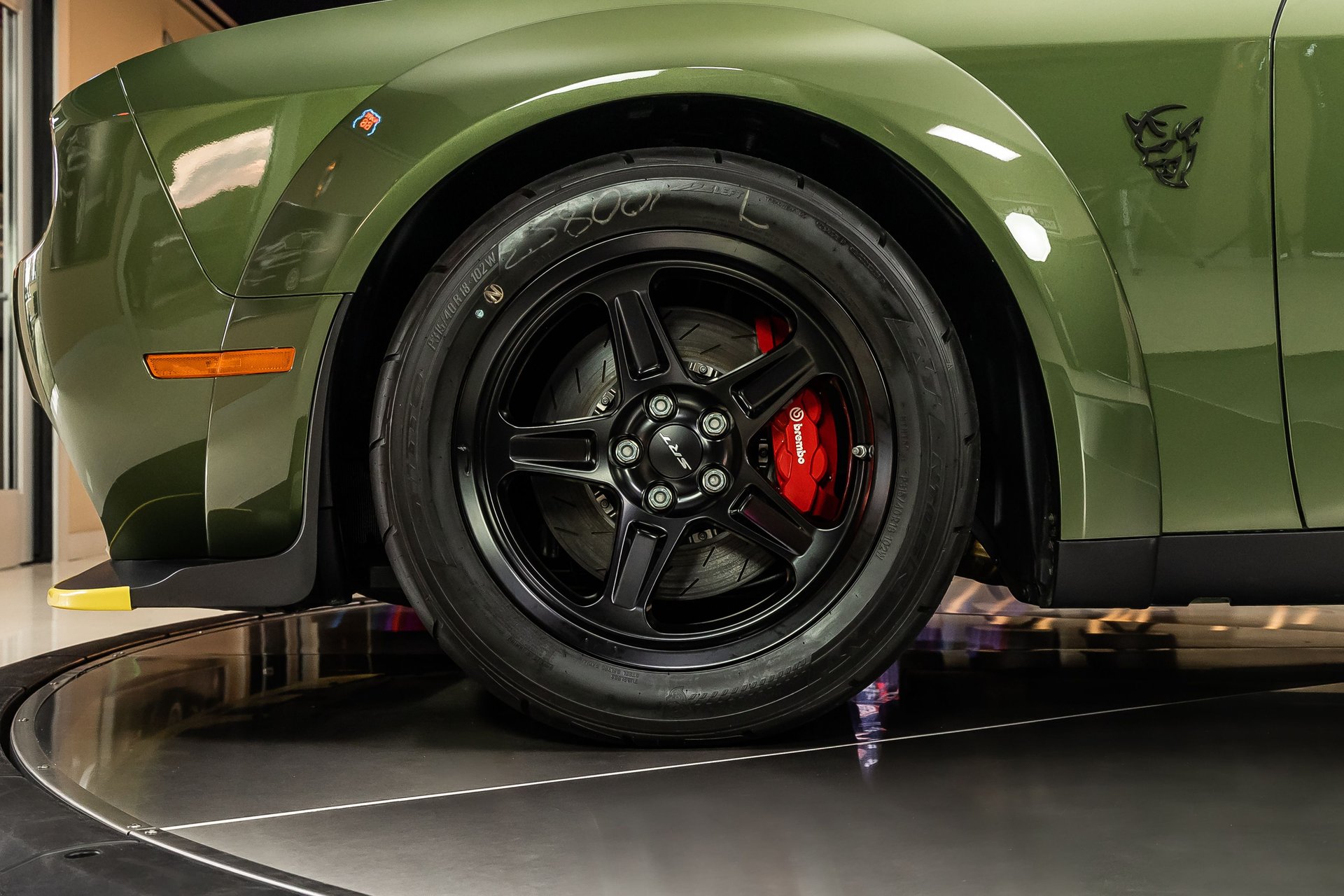 A close-up of the front wheel and fender of a green Dodge Challenger SRT Demon on a turntable.