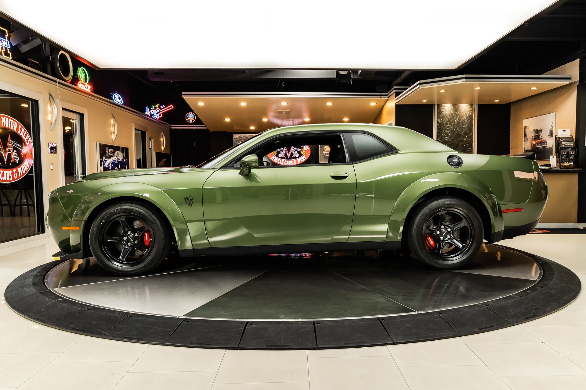 A side profile view of a green Dodge Challenger on a rotating display platform in a showroom.