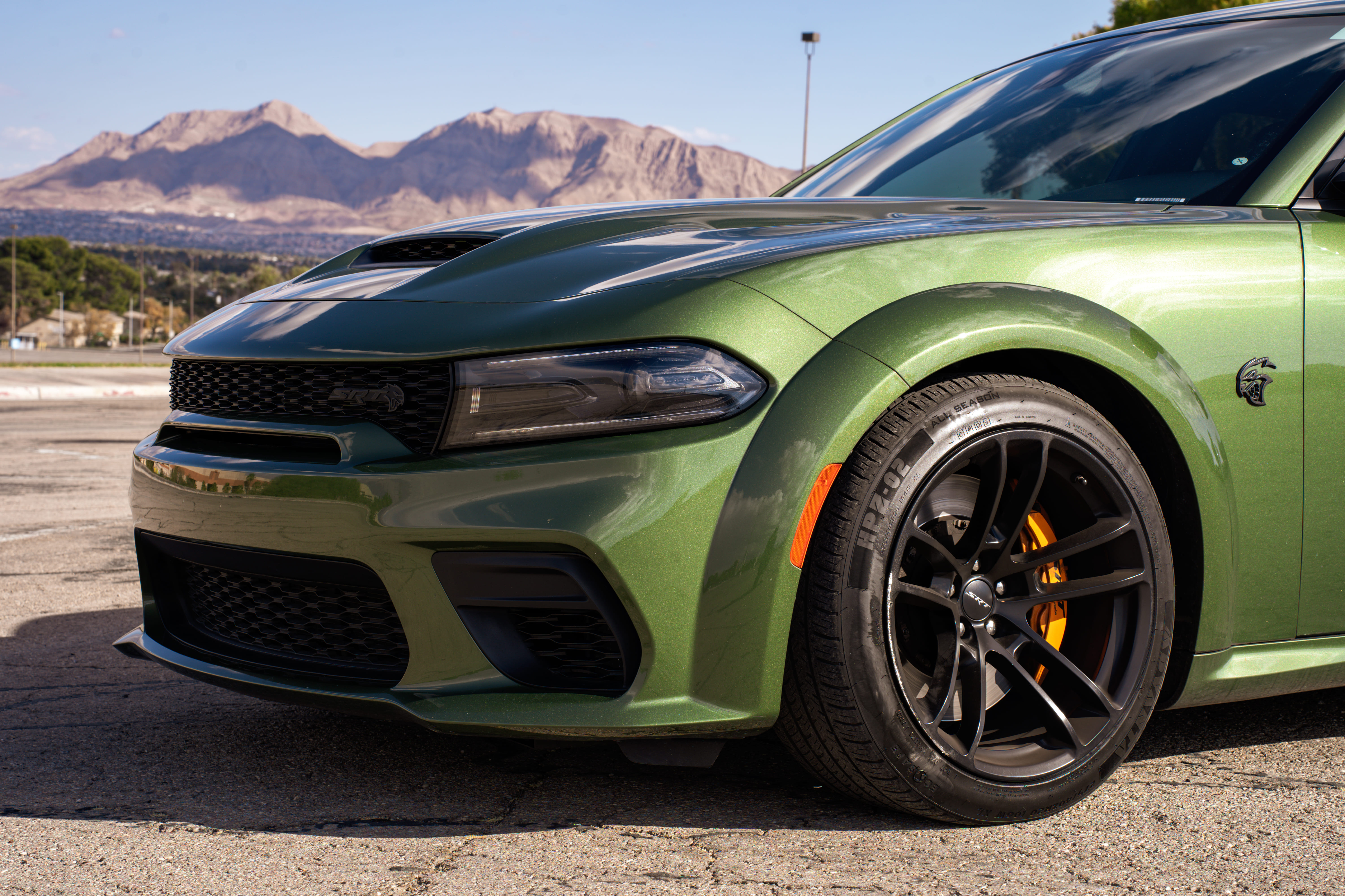 A close-up of the front of a green Dodge Charger Hellcat with mountains in the background.