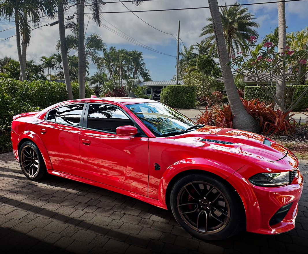 Red sports car parked on a driveway with palm trees in the background.
