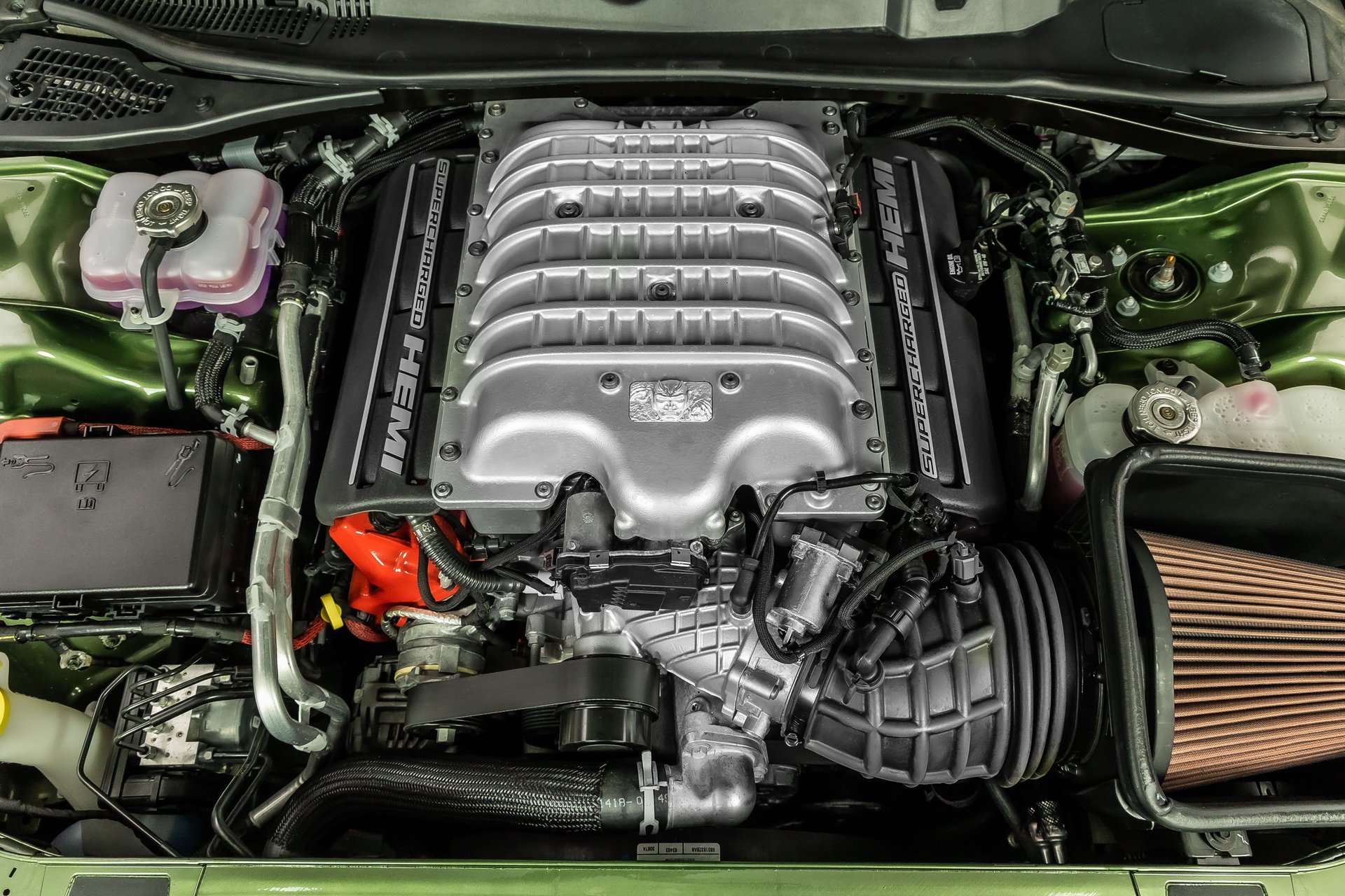 An overhead view of a clean, silver supercharged HEMI engine inside a car's green engine bay.