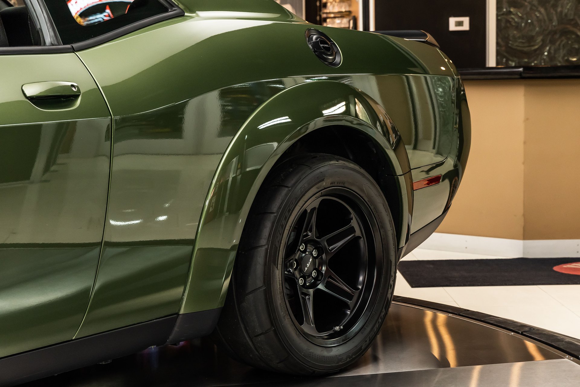 A close-up of the rear quarter panel of a dark green Dodge Challenger with black wheels.