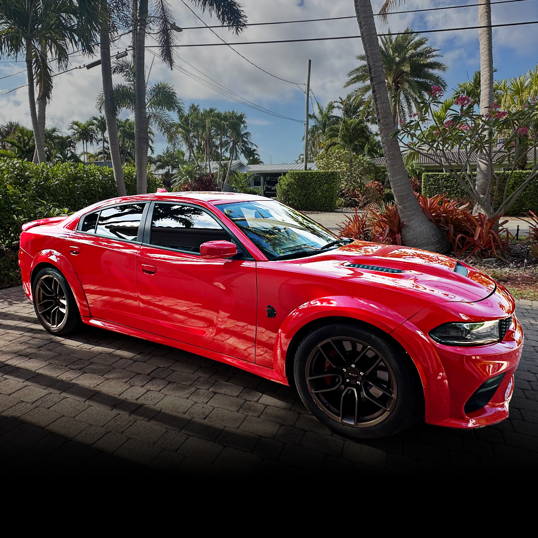 Red sports car parked on a driveway with palm trees in the background.