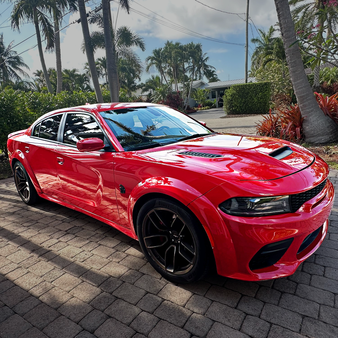 Red sports car parked on a paved driveway with palm trees in the background.