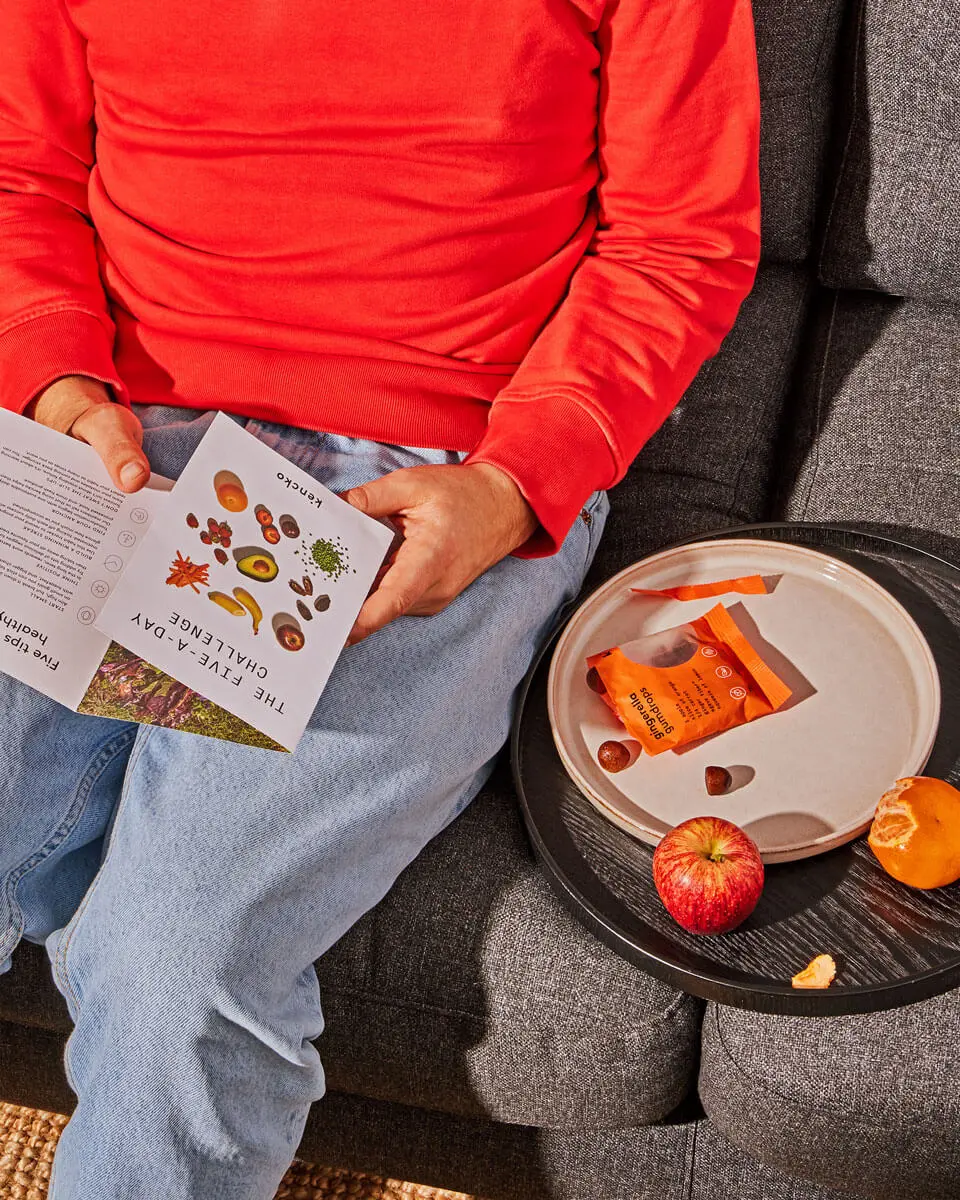 Person in red sweater reading a booklet, with fruit and snacks on a tray.