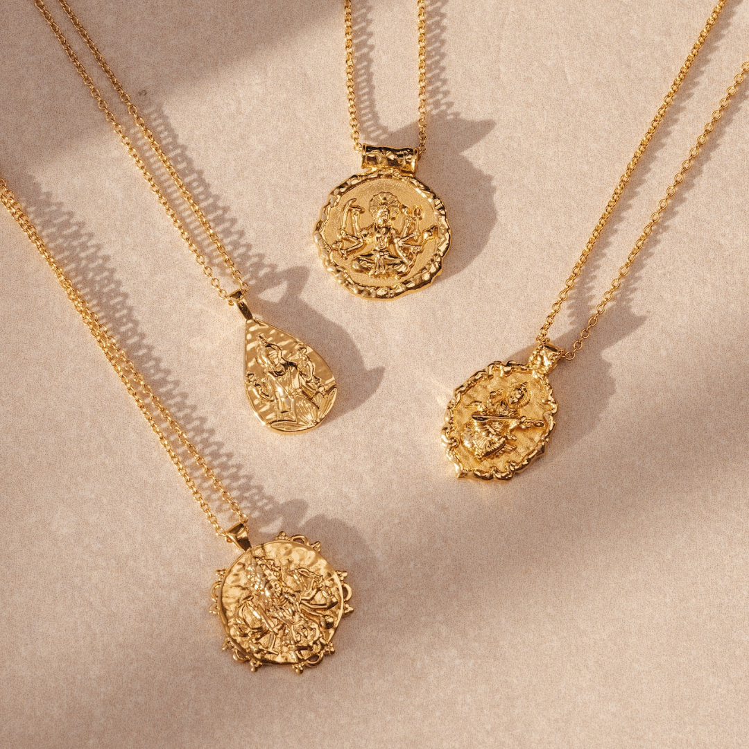 Four gold necklaces with intricate pendant designs on a beige background.