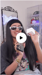 A woman in sunglasses and a headband holds a smartphone and a small white box, smiling at the camera.