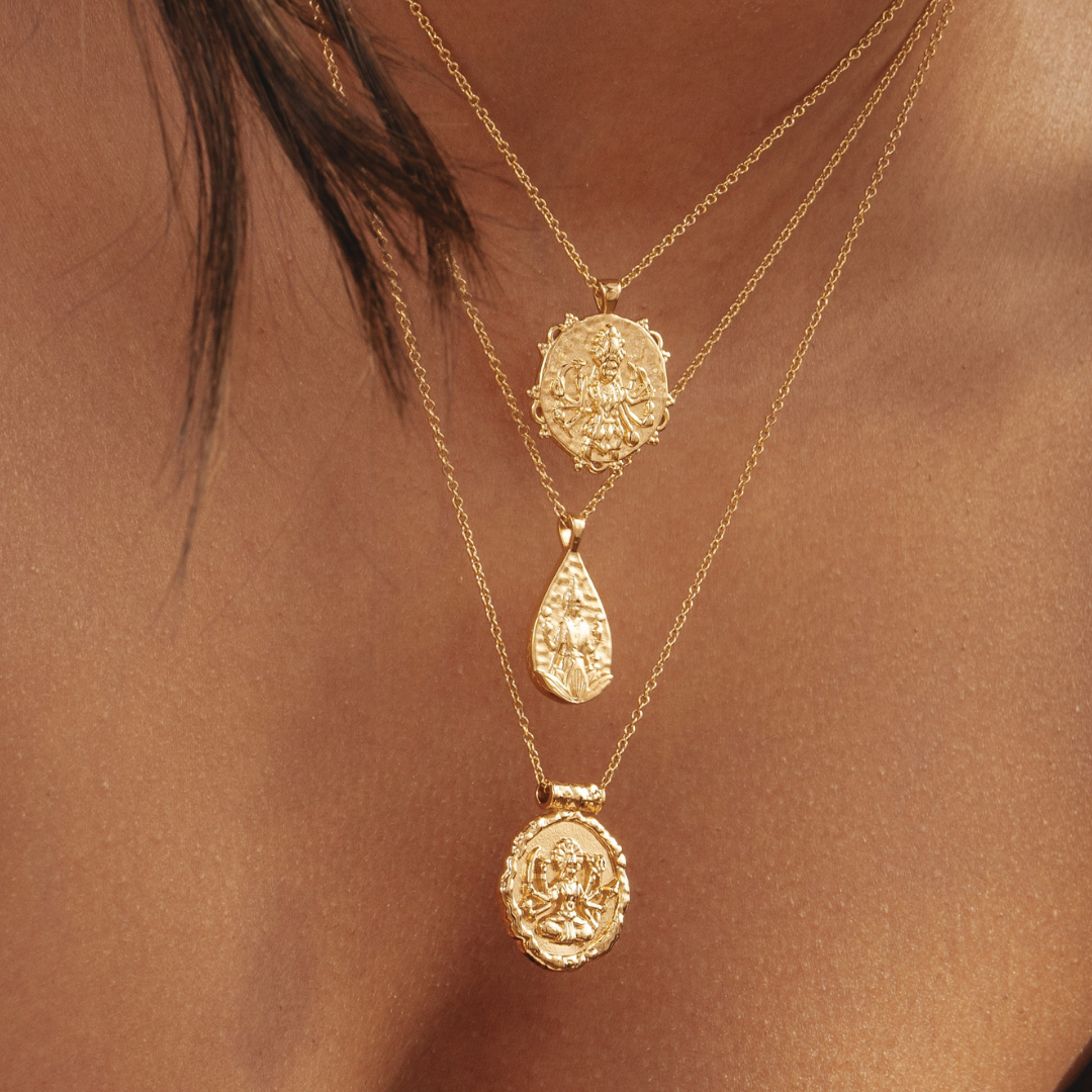 Three layered gold necklaces with intricate pendants on a person's neck.