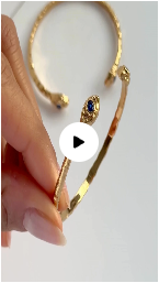 A hand holds a gold-colored snake bracelet with a blue gem eye, with a video play icon overlay.