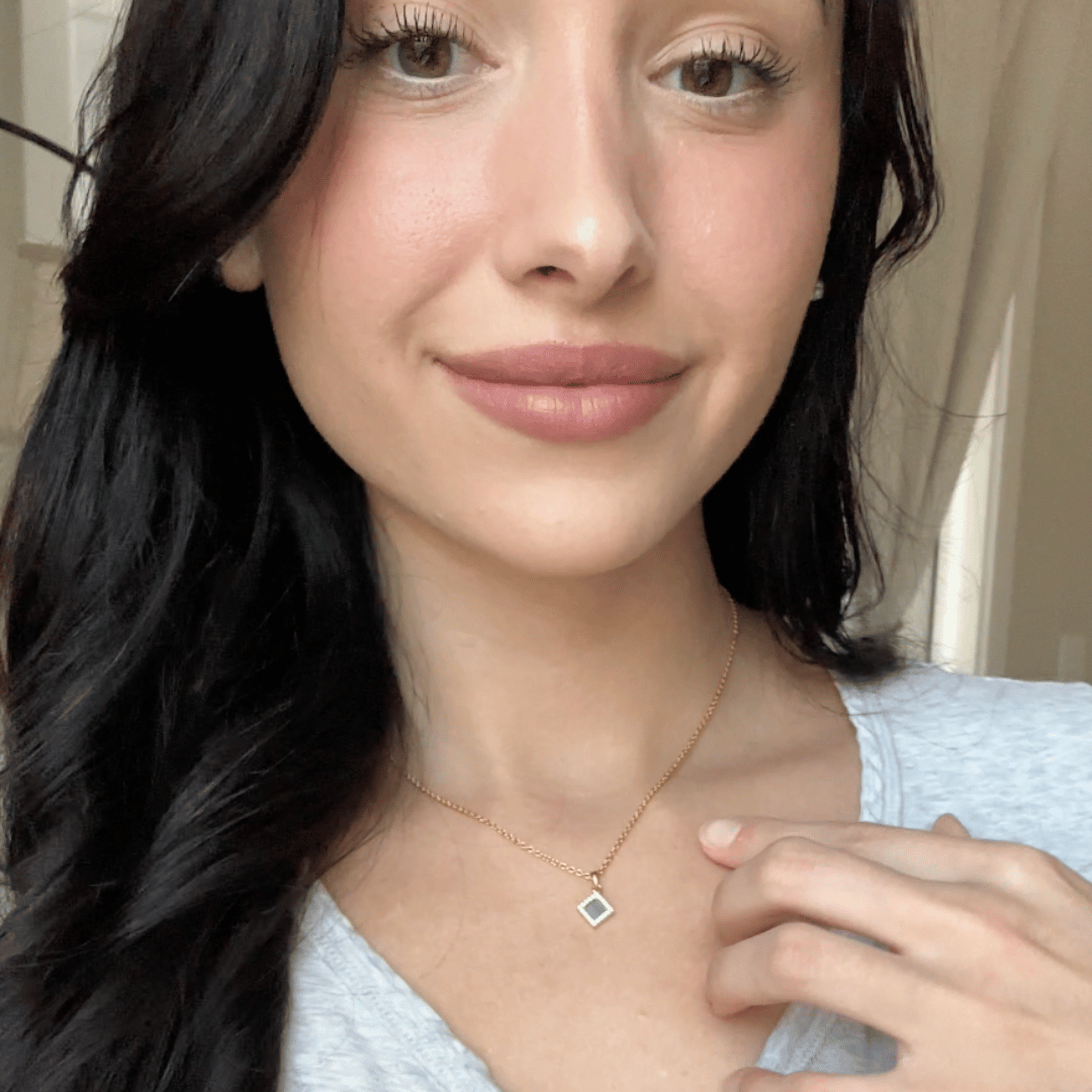 Person with long dark hair wearing a necklace and a light-colored top.