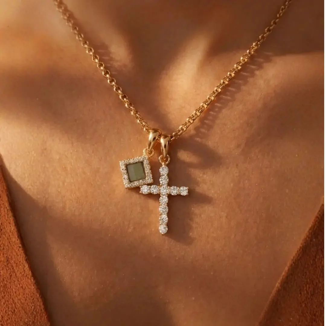 A gold chain necklace with a diamond cross and a square gemstone pendant on a person's neck.
