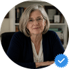 A headshot of a woman with gray hair and glasses, with a blue verified checkmark badge in the corner.