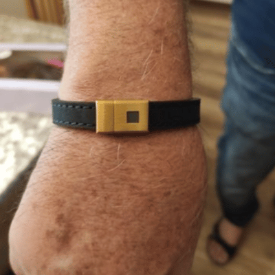 A person wearing a black leather bracelet with a gold clasp.