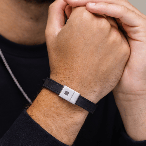 Person wearing a black wristband with a square metallic clasp.