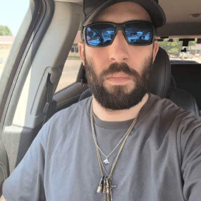 Man with sunglasses and a beard sitting in a car.