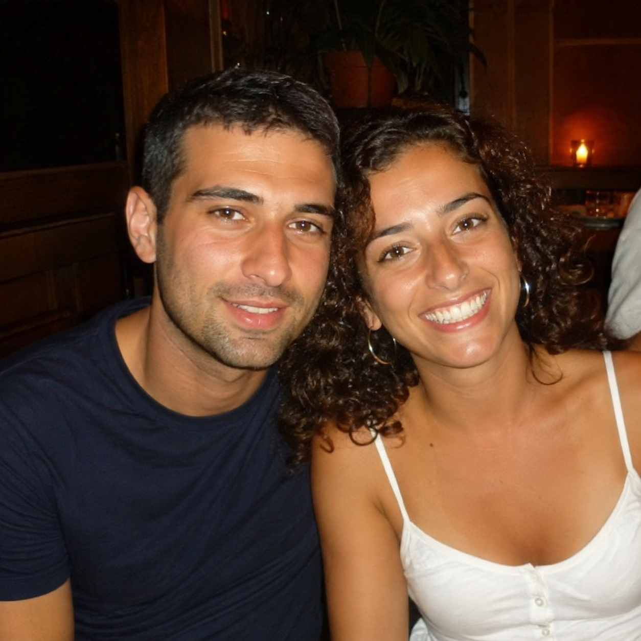 A smiling man and woman with dark hair pose for a photo in a dimly lit restaurant.