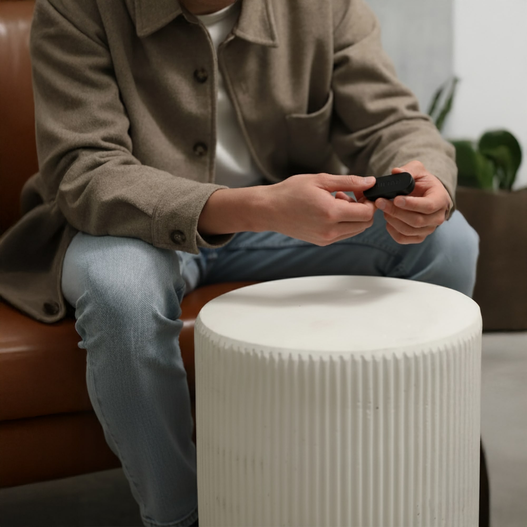 Person in brown jacket holding an object, sitting on a sofa beside a white table.