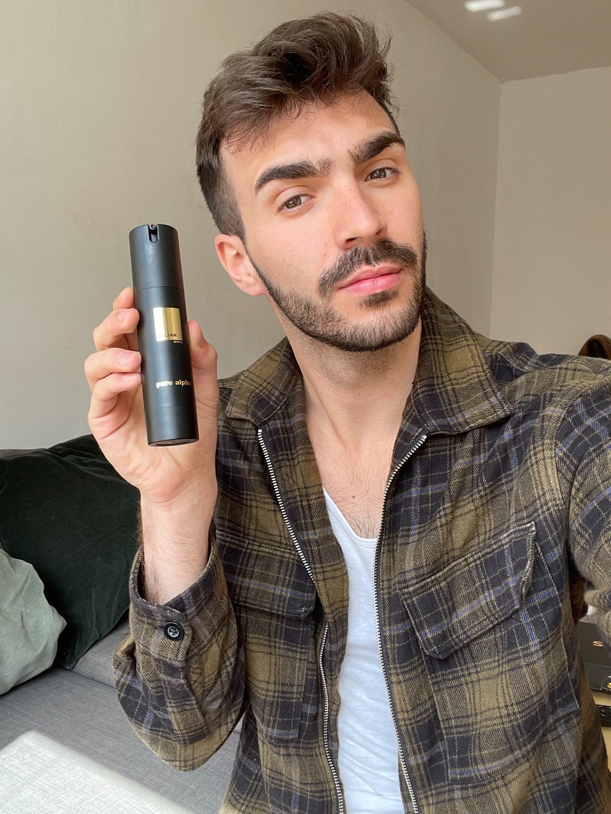 Person holding a black spray bottle indoors, wearing a plaid shirt.