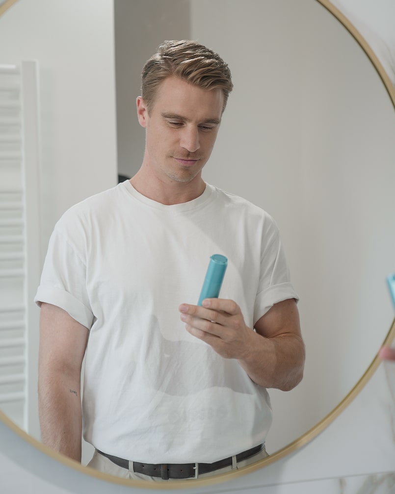 Man in white shirt looking at a blue bottle in a mirror reflection.