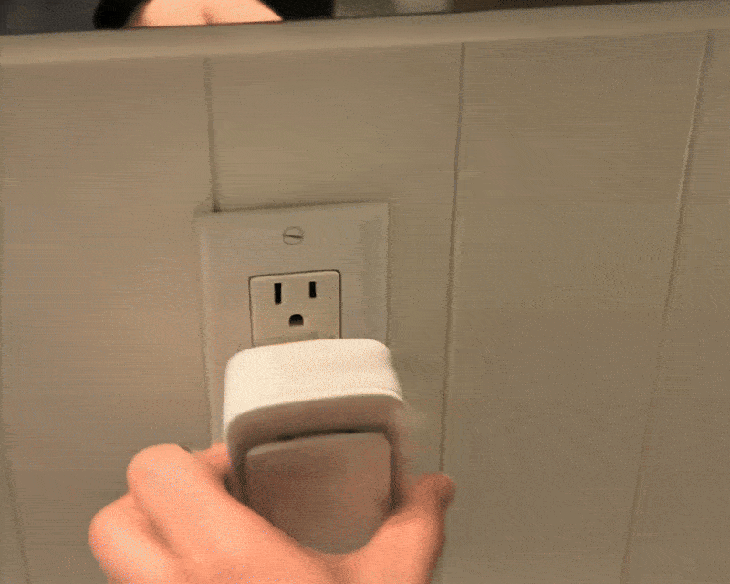 Hand plugging a device into a wall outlet.