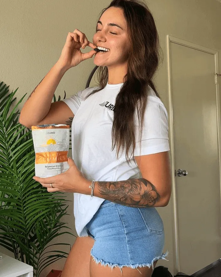 Person eating from a snack bag, standing indoors with a plant in the background.