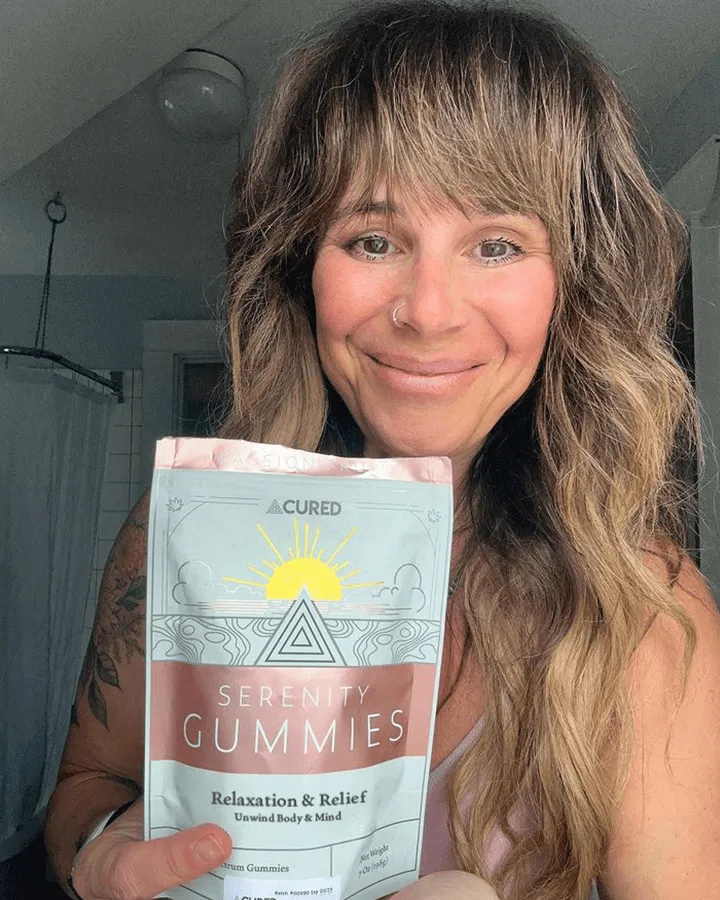 Person holding a package of Serenity Gummies, smiling indoors.