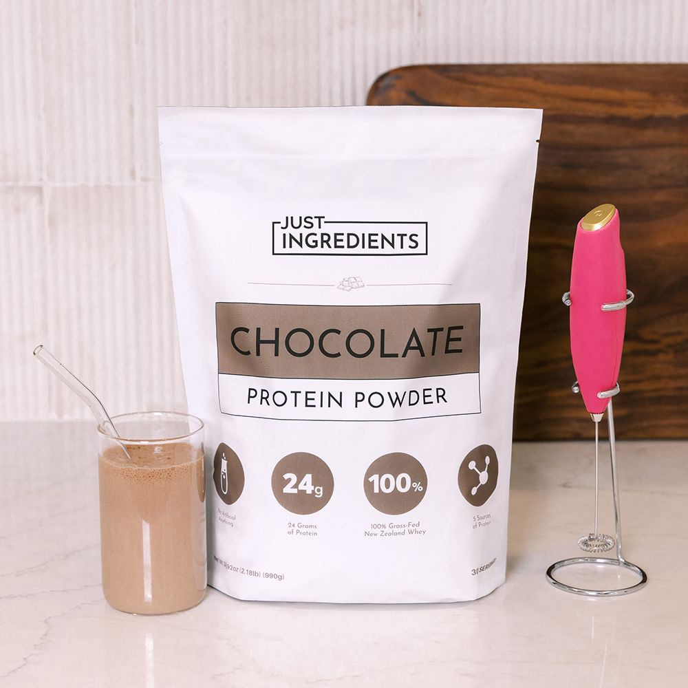 Bag of chocolate protein powder with a glass of shake and a pink frother.