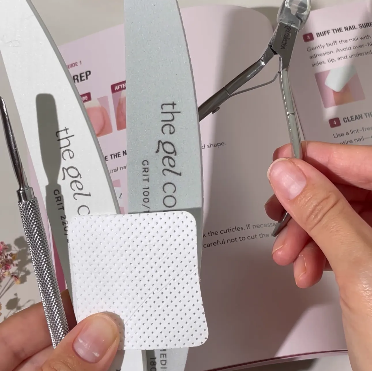 A person holding various manicure tools, including nail files, cuticle nippers, and a wipe, over an instruction booklet.