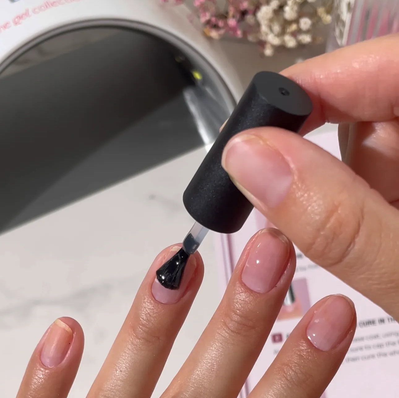 A close-up of a person applying clear gel polish to a fingernail with a brush.