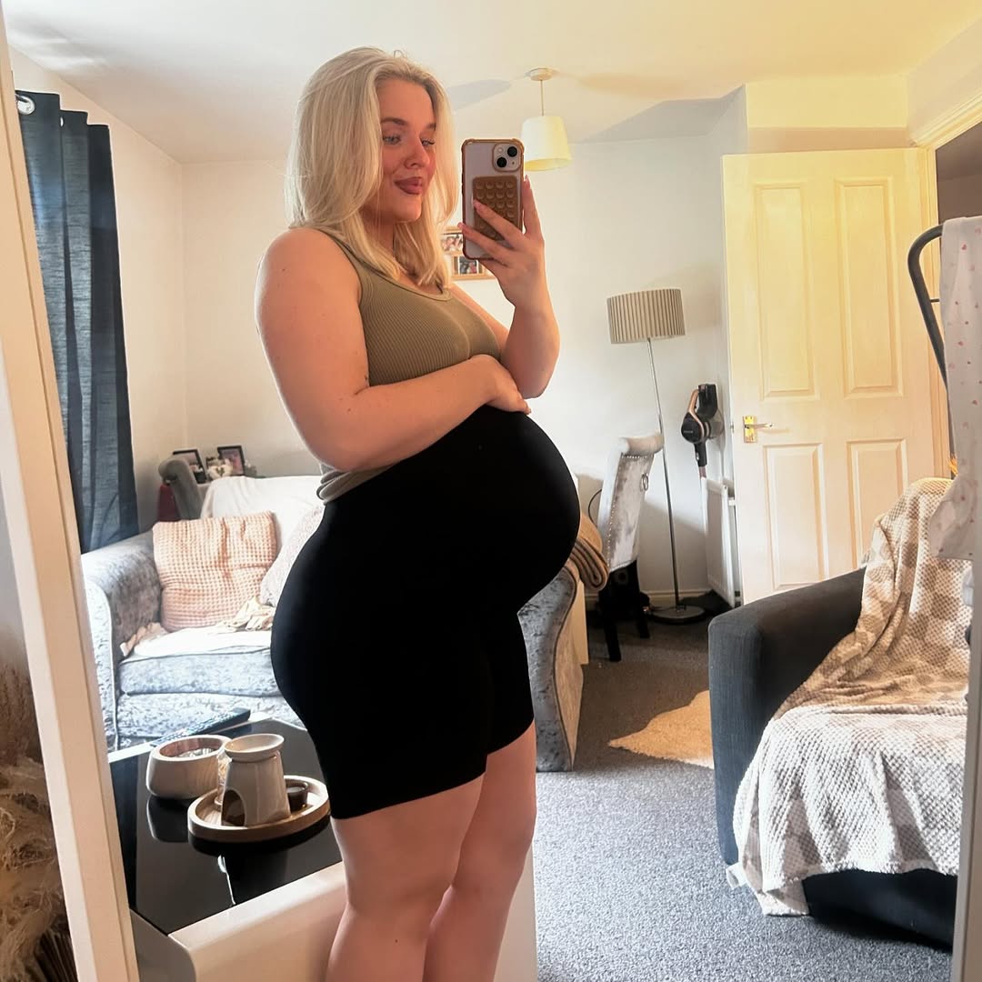 Pregnant woman taking a mirror selfie in a living room.