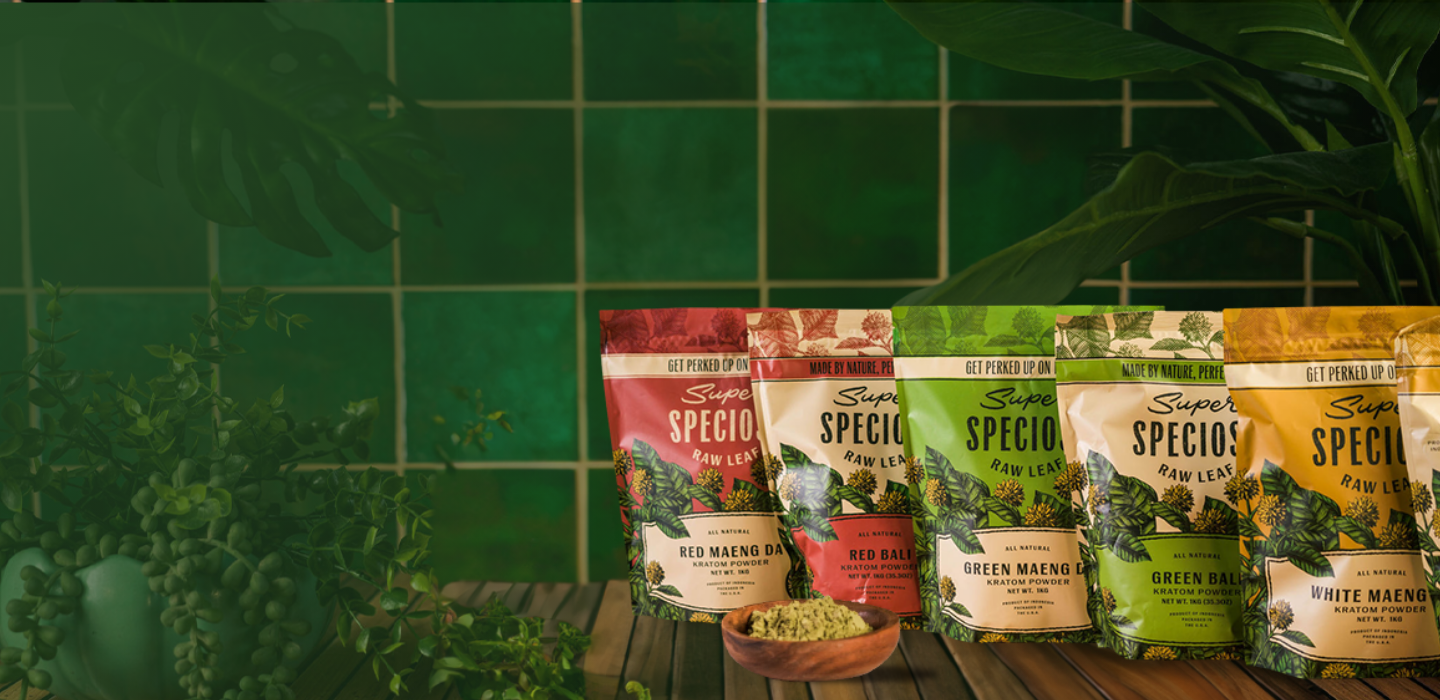 Four bags of kratom powder on a wooden surface with a green tiled background.