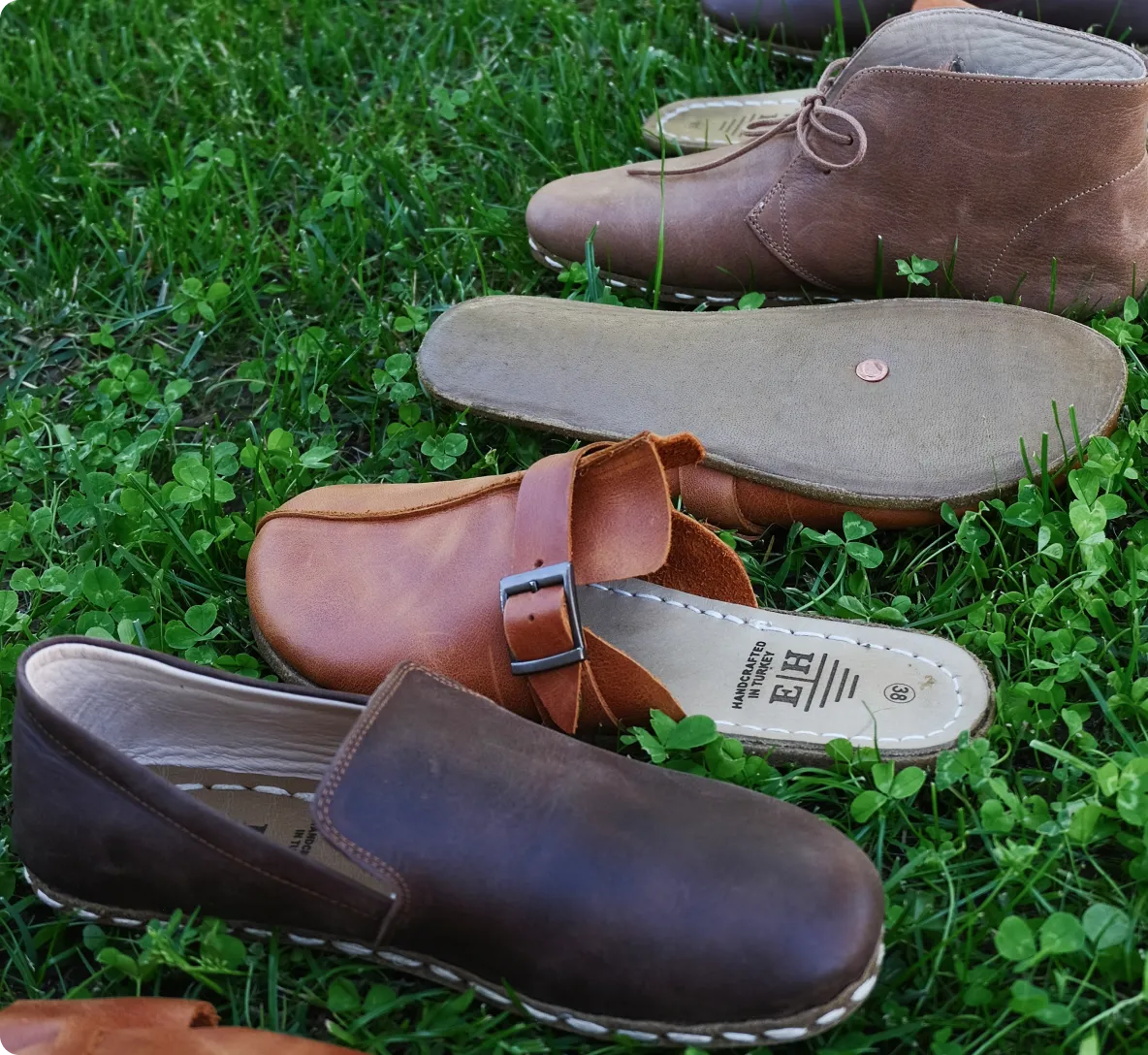 Assorted brown leather shoes displayed on green grass.