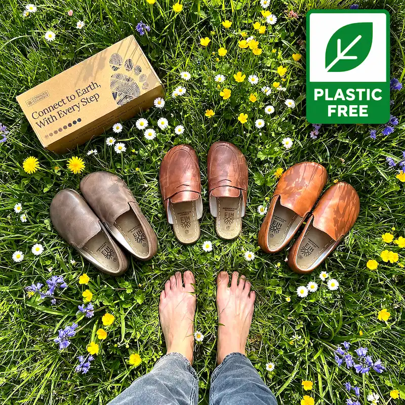 Overhead view of bare feet, three pairs of shoes, and a box on a grassy field with wildflowers.
