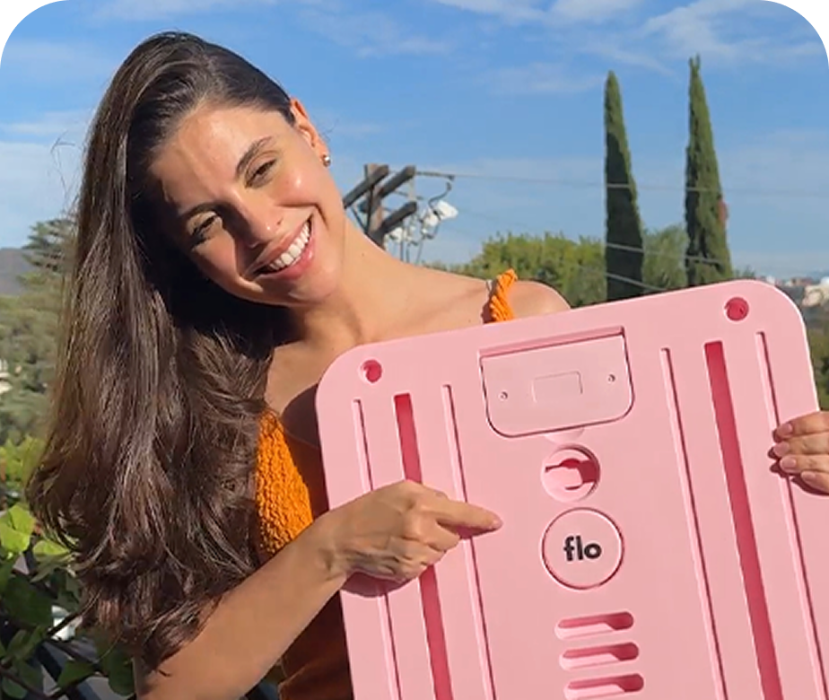 A smiling woman outdoors holds a large pink product and points to the 'flo' logo.