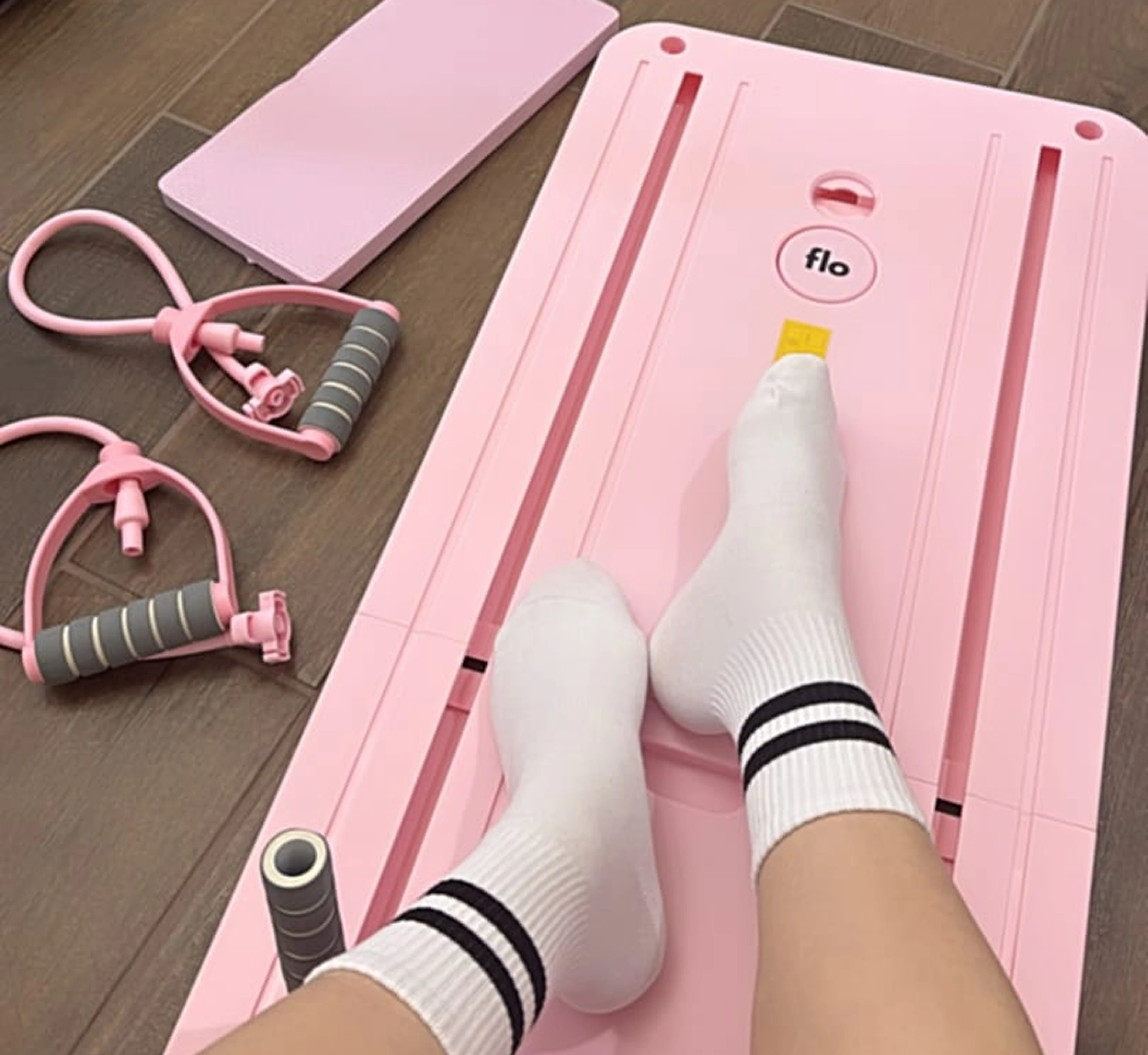 A person's feet in striped socks on a pink 'flo' exercise board with matching workout accessories.