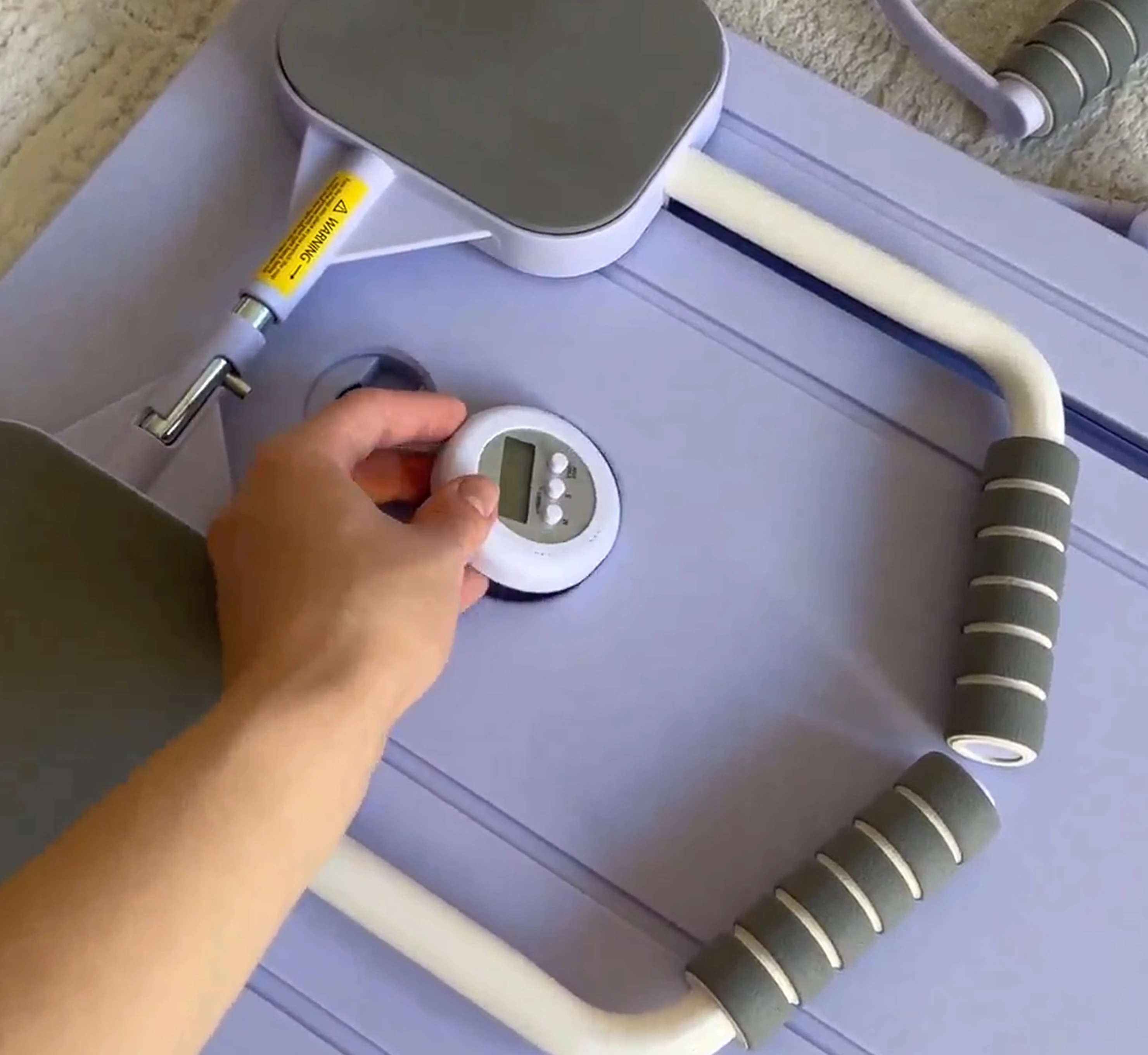 A person places a small digital timer onto a purple piece of home exercise equipment.