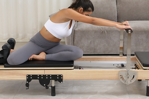 Person exercising on a Pilates reformer machine in a living room setting.