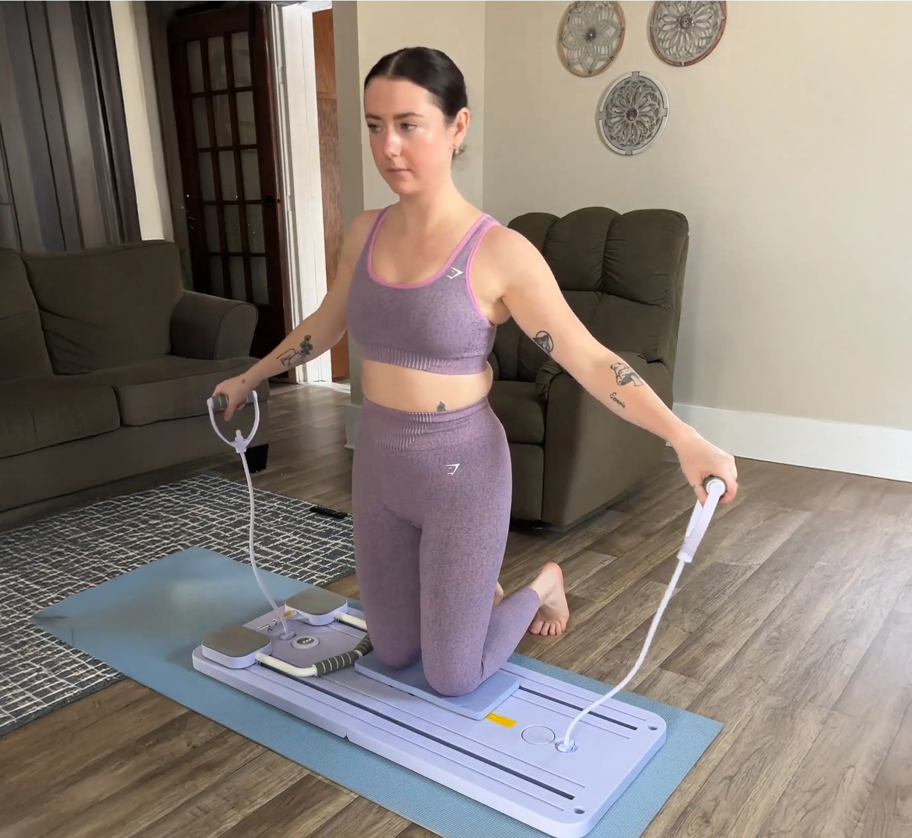 A woman in purple workout clothes exercises at home, kneeling on a resistance training board.