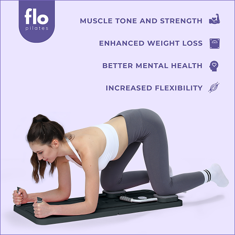 A woman in a pink outfit kneels on a wooden Pilates reformer, stretching her arms overhead with straps.