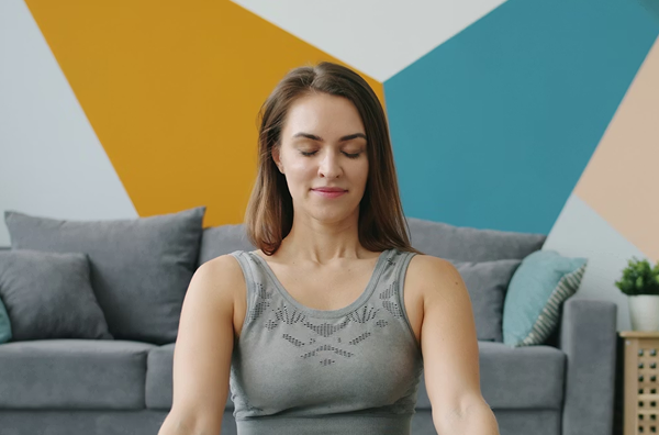 A woman sitting on a couch with eyes closed, colorful wall in background.